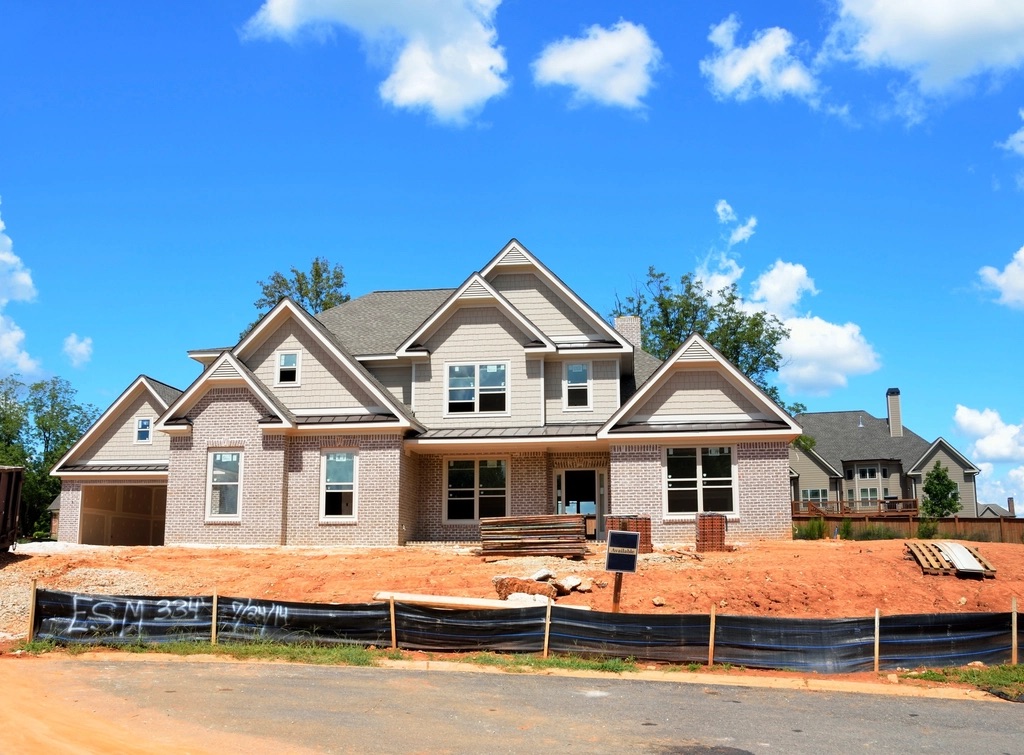 A finished new brick house on a bare dirt lot with a sign post out front