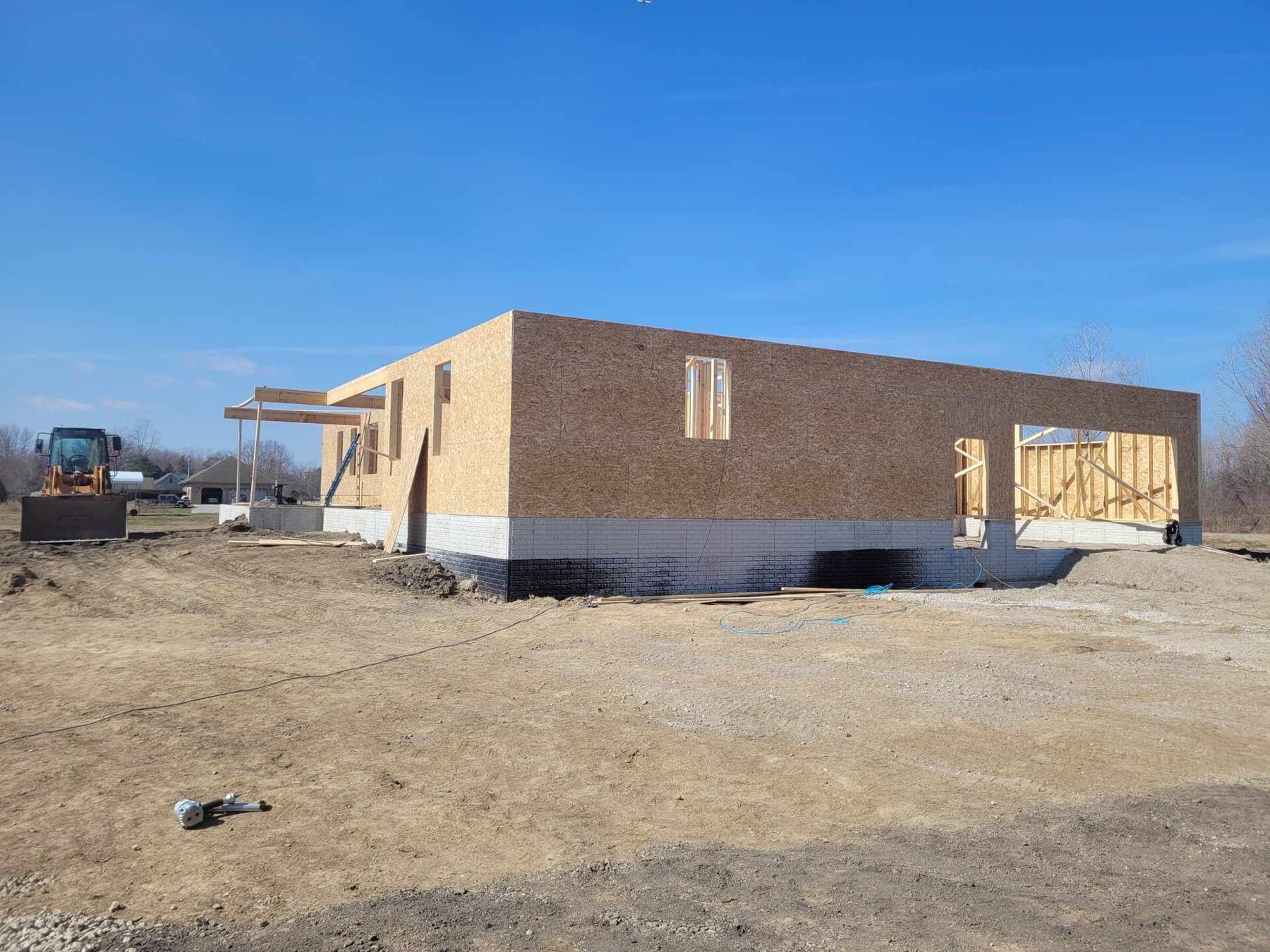 A single-storey house in sheathing on a fresh slab, with a loader parked beside it
